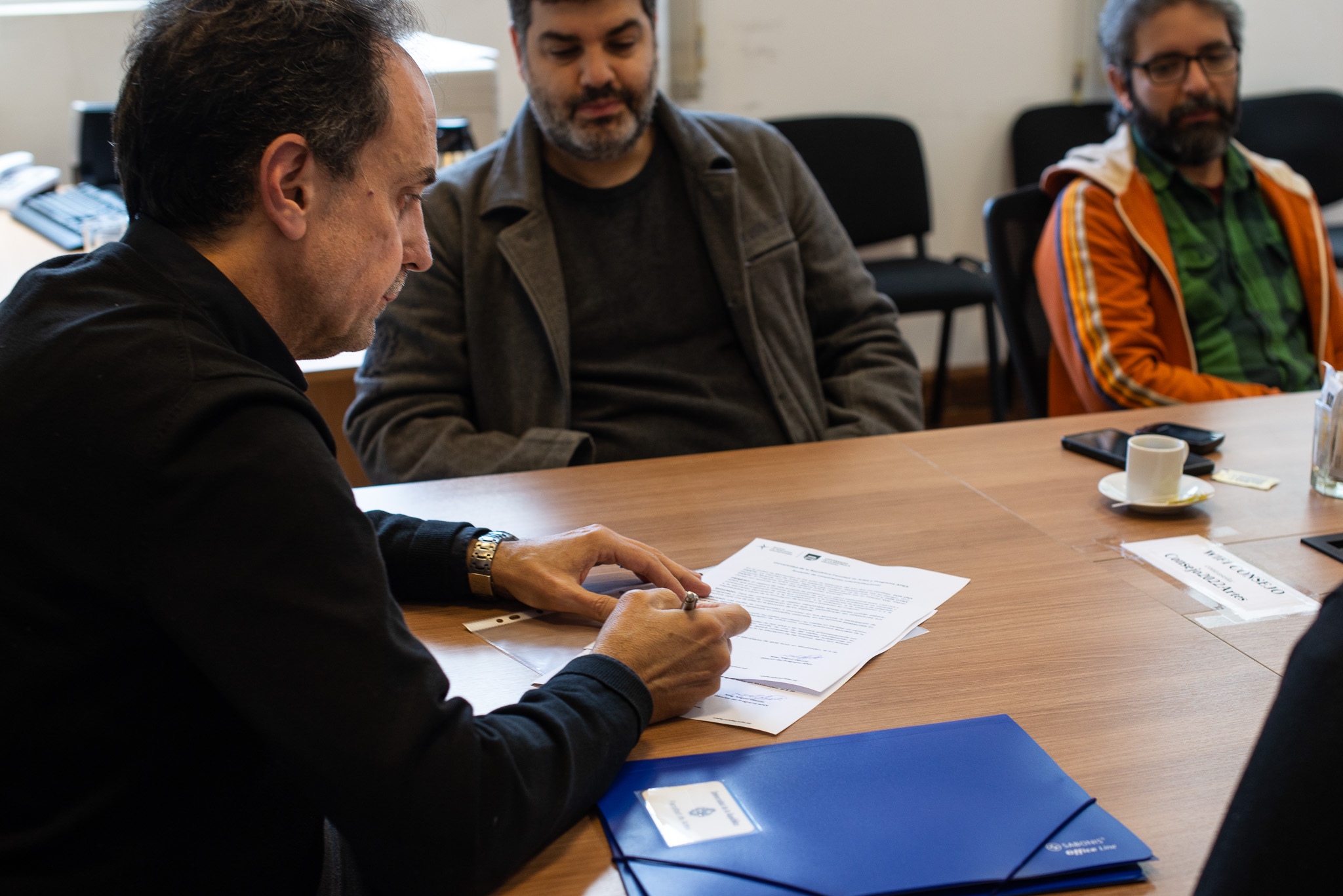 En la fotografía se ve a Fernando Miranda firmando el acuerdo interinstitucional y de frente sentados en la mesa se ve a Miguel Olivetti y a Pablo Pereira.