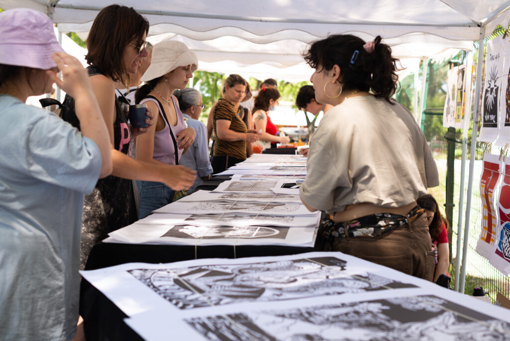 Fotografía donde se ven varias personas alrededor del stand de artes gráficas y se pueden apreciar las obras en xilografía.