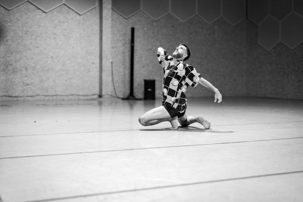 Lucas Condró realiza una pose expresiva, en el centro de una sala de danza. La escena es en blanco y negro.