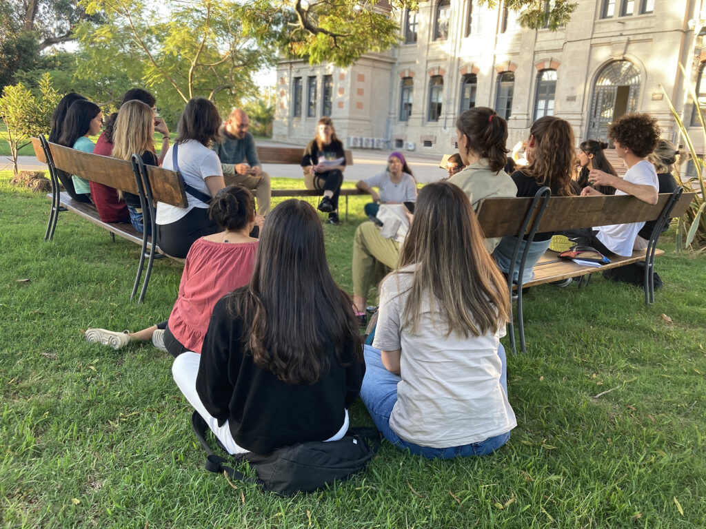 Grupo de estudiantes y docentes sentados en ronda al aire libre, participando en una instancia de intercambio y trabajo colectivo.