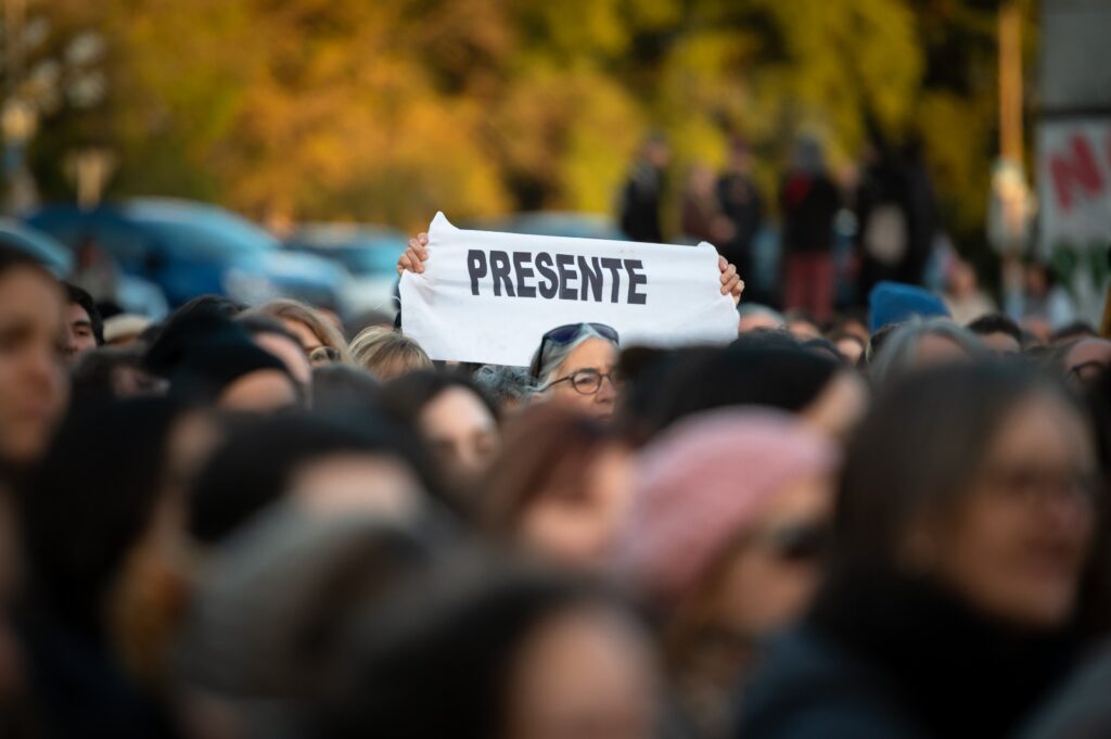 WhatsApp Image 2026-05-14 at 11.34.17 PM Persona sostiene un cartel en la multitud que dice "Presente"
