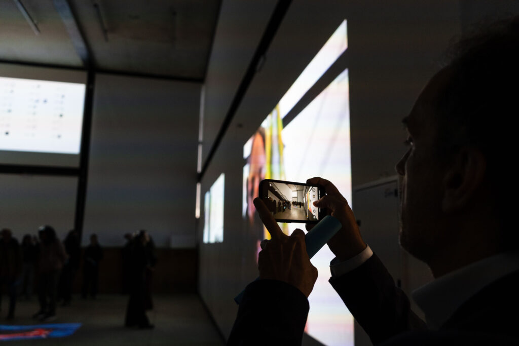 Arte a través de los océanos. Se ve una persona con celular tomando una foto de la muestra